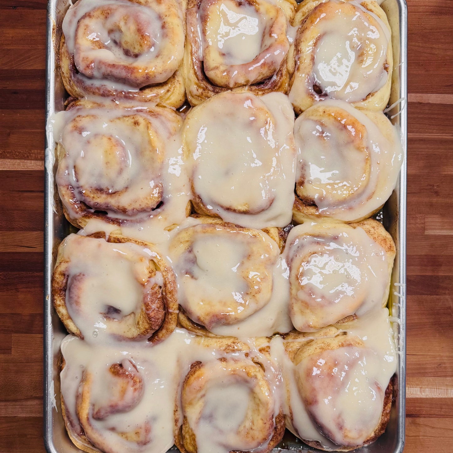Tray of cinnamon rolls with icing on a wooden surface